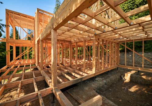 Wooden frame house under construction near forest.